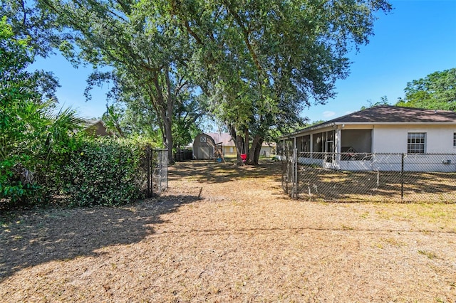view of yard featuring a fenced backyard, a storage unit, an outdoor structure, and a sunroom