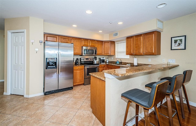 kitchen featuring visible vents, a peninsula, brown cabinets, and stainless steel appliances