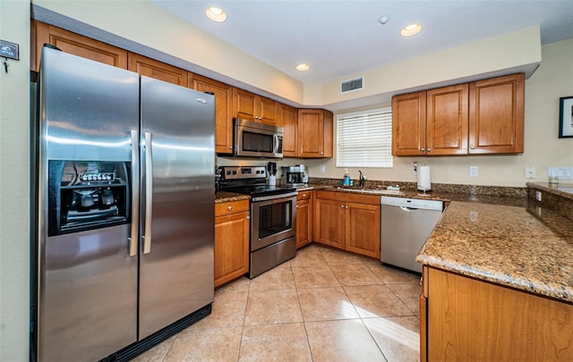 kitchen featuring appliances with stainless steel finishes, brown cabinetry, dark stone counters, light tile patterned floors, and visible vents