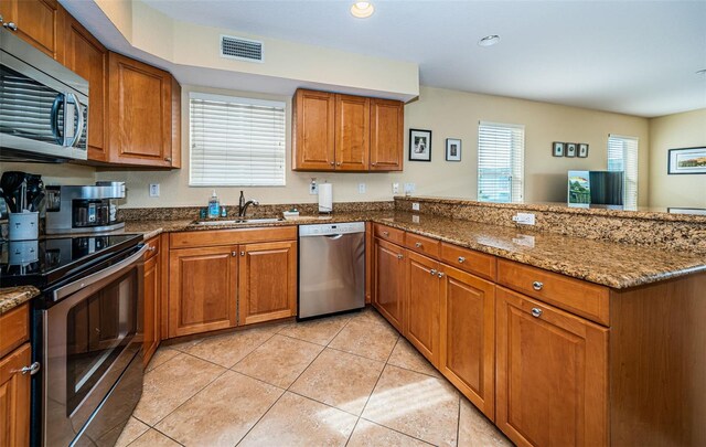 kitchen with brown cabinetry, a sink, a peninsula, and stainless steel appliances