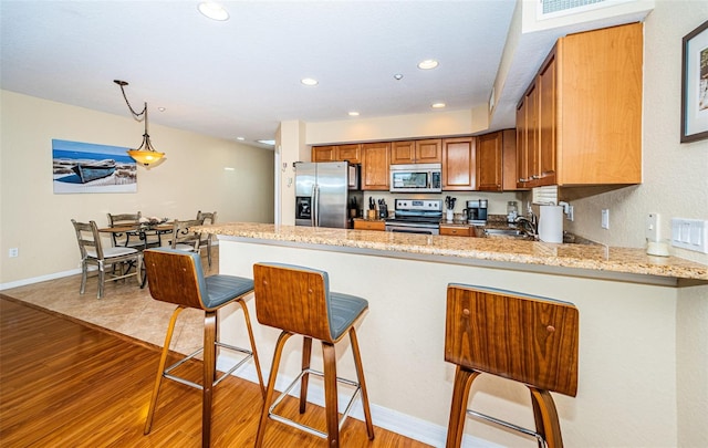 kitchen featuring brown cabinetry, a sink, a peninsula, light wood finished floors, and stainless steel appliances