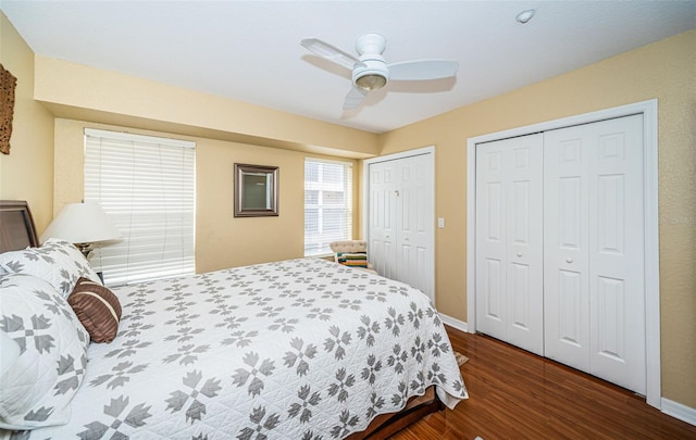 bedroom with two closets, dark wood-style flooring, baseboards, and a ceiling fan