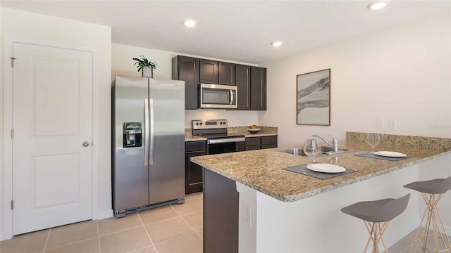 kitchen featuring a sink, a breakfast bar area, stainless steel appliances, a peninsula, and light tile patterned floors