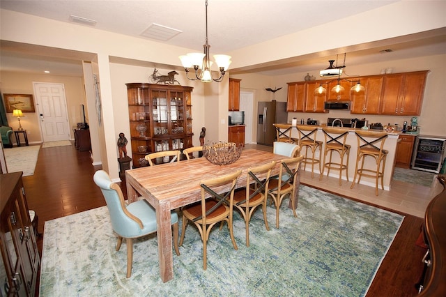dining room with a notable chandelier, light wood-style flooring, visible vents, and wine cooler
