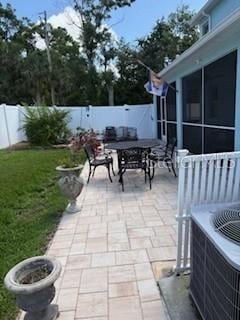 view of patio / terrace featuring a sunroom, central AC unit, outdoor dining area, and a fenced backyard