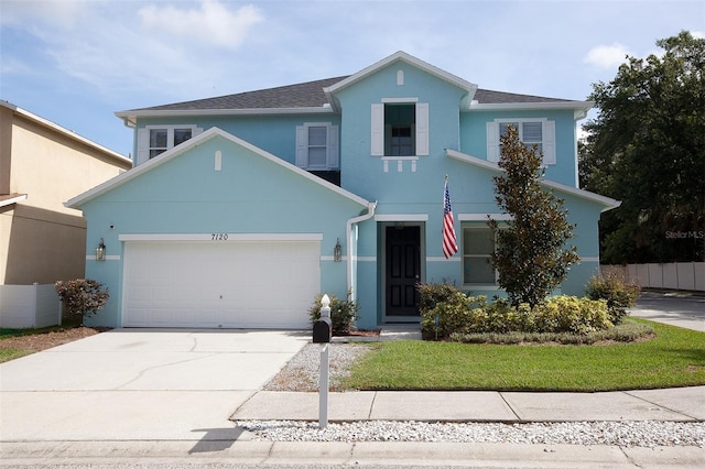 view of front of property with concrete driveway, an attached garage, a front lawn, and stucco siding