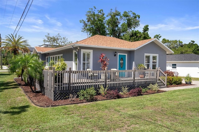 ranch-style home featuring a deck, stucco siding, a front lawn, and a shingled roof