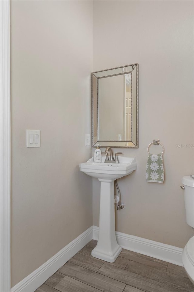 half bathroom featuring toilet, wood finished floors, and baseboards