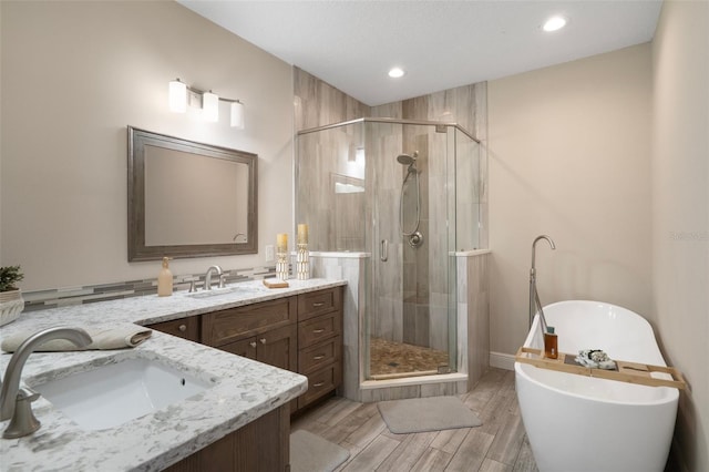 bathroom featuring vanity, a soaking tub, a stall shower, wood finished floors, and recessed lighting