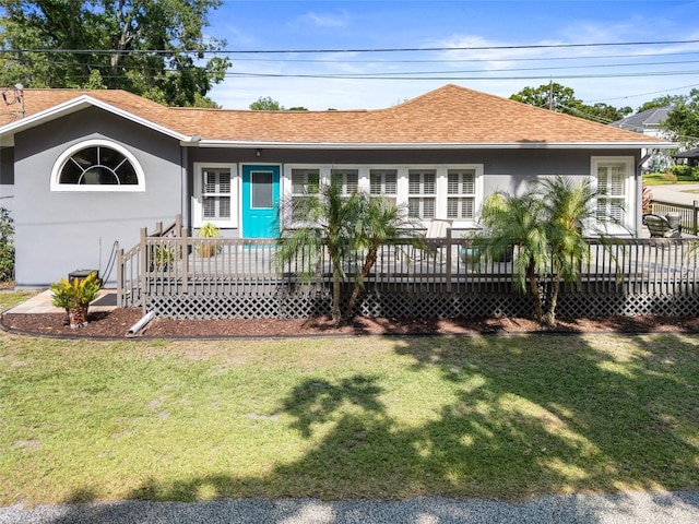 view of front facade featuring roof with shingles, a front lawn, stucco siding, and a deck