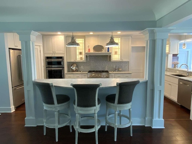 kitchen featuring appliances with stainless steel finishes, a sink, white cabinetry, backsplash, and ornate columns