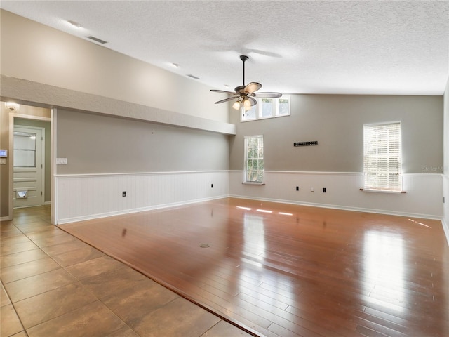 unfurnished living room featuring a wainscoted wall, a textured ceiling, visible vents, and ceiling fan