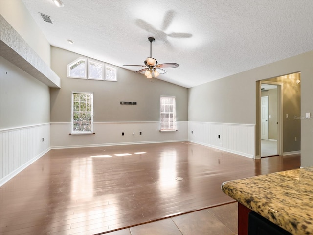 unfurnished living room featuring a textured ceiling, wainscoting, visible vents, ceiling fan, and wood finished floors