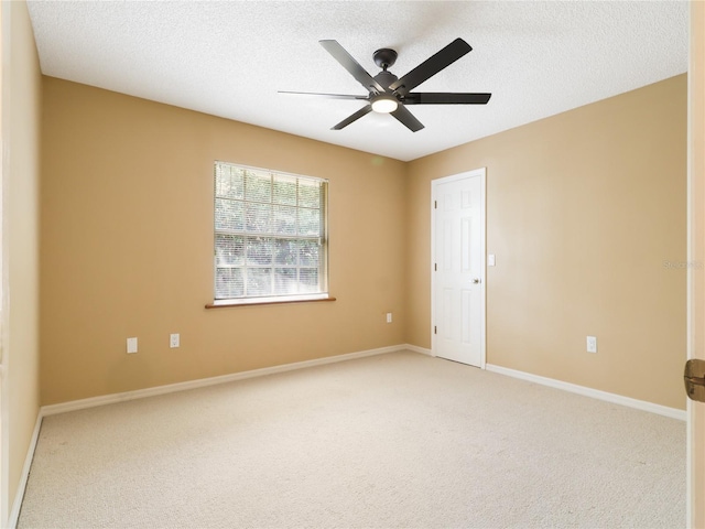 spare room featuring light colored carpet, a textured ceiling, baseboards, and a ceiling fan