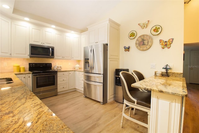 kitchen featuring appliances with stainless steel finishes, light wood finished floors, tasteful backsplash, a kitchen breakfast bar, and recessed lighting