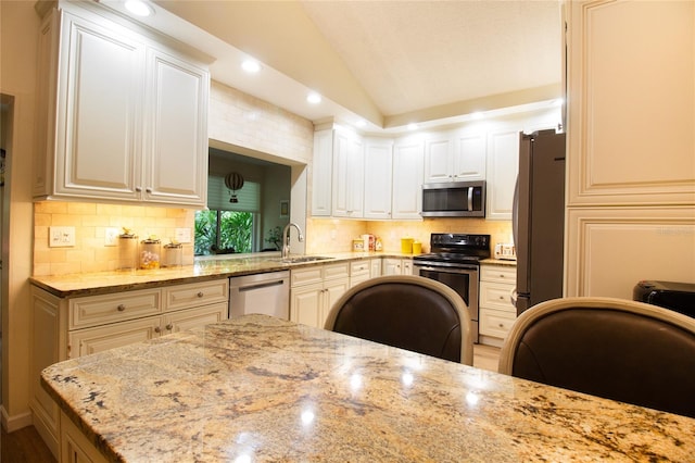 kitchen featuring stainless steel appliances, vaulted ceiling, a sink, decorative backsplash, and light stone countertops
