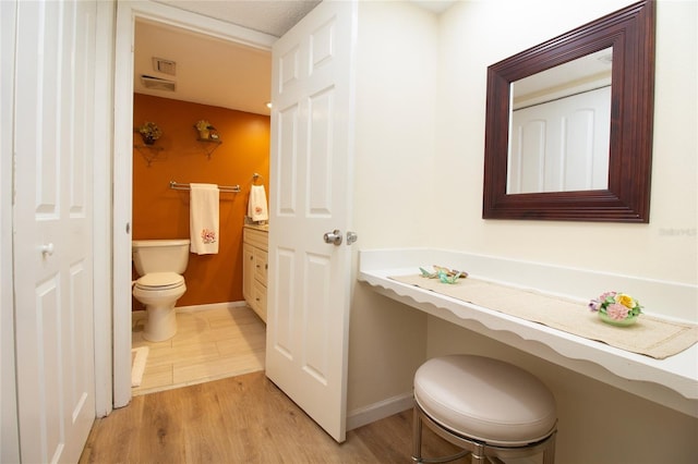 half bathroom featuring wood finished floors, toilet, baseboards, and vanity