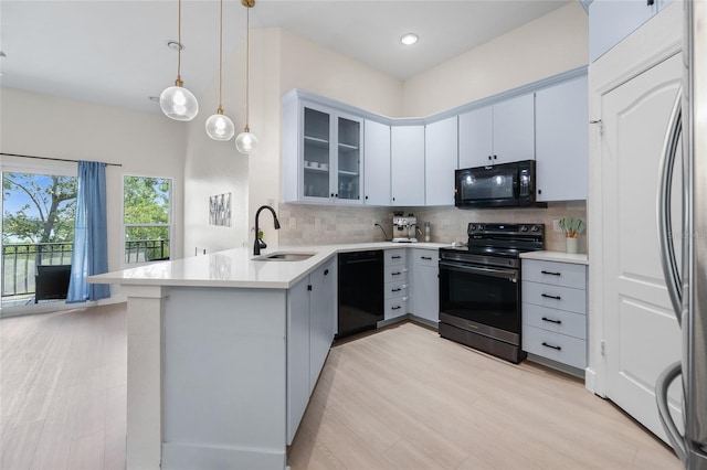 kitchen with a sink, a peninsula, backsplash, glass insert cabinets, and black appliances