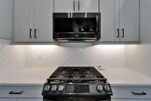 5828 Clairwood Ct, Palmetto, FL 34221 - kitchen with black gas range, stainless steel microwave, decorative backsplash, and light stone countertops