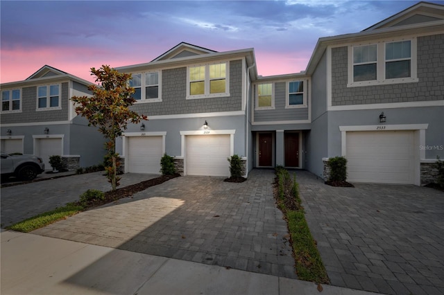 townhome / multi-family property with stone siding, stucco siding, driveway, and a garage