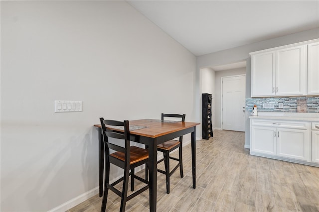 dining space featuring baseboards, light wood-style flooring, and lofted ceiling