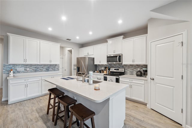 kitchen with a kitchen island with sink, appliances with stainless steel finishes, tasteful backsplash, and a sink
