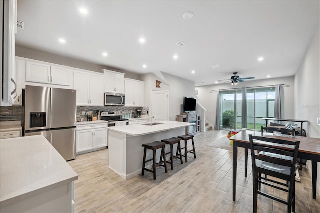kitchen with a sink, stainless steel appliances, a breakfast bar, white cabinetry, and decorative backsplash