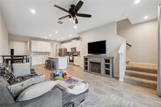 living area with stairs, recessed lighting, ceiling fan, light wood finished floors, and baseboards