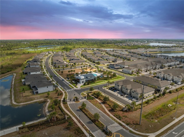 aerial view at dusk with a water view and a residential view