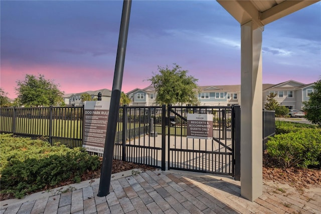 gate at dusk featuring fence and a residential view