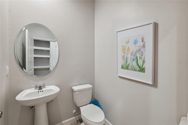 half bath with toilet, baseboards, and a sink