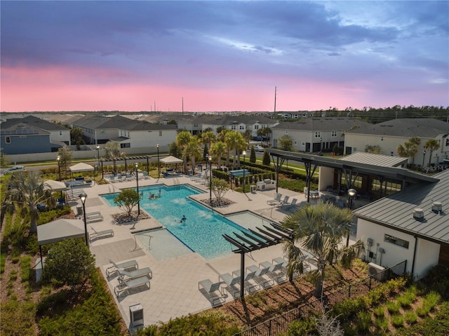 pool at dusk featuring fence, a patio, a community pool, and a residential view