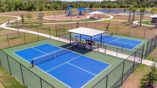view of tennis court featuring fence, a water view, a yard, and playground community