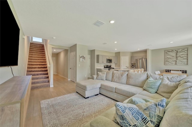 living area featuring recessed lighting, baseboards, light wood-type flooring, visible vents, and stairway