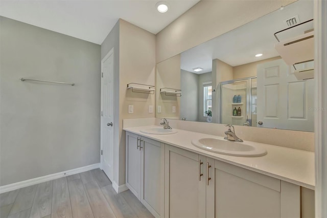 bathroom with a sink, double vanity, a stall shower, and wood finished floors