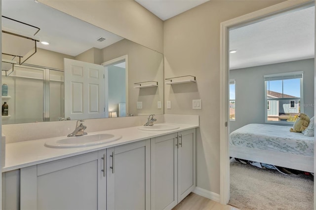 ensuite bathroom featuring connected bathroom, double vanity, baseboards, and a sink