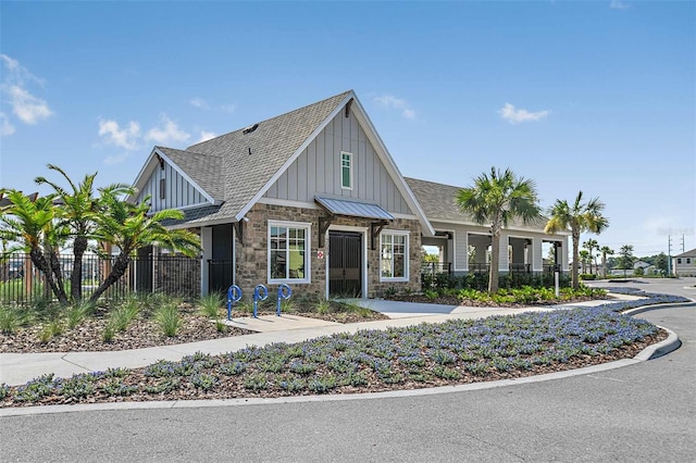 craftsman-style home featuring fence, board and batten siding, roof with shingles, and stone siding