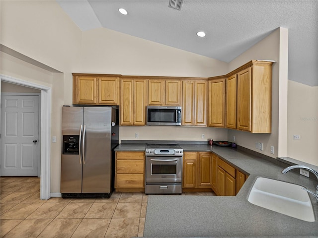 kitchen featuring a sink, lofted ceiling, light tile patterned flooring, dark countertops, and appliances with stainless steel finishes