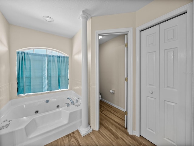 bathroom with toilet, a jetted tub, a closet, and wood finished floors