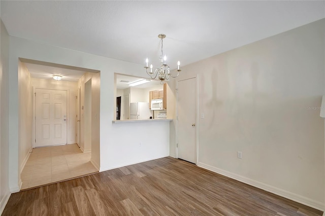 unfurnished dining area featuring a chandelier, wood finished floors, and baseboards
