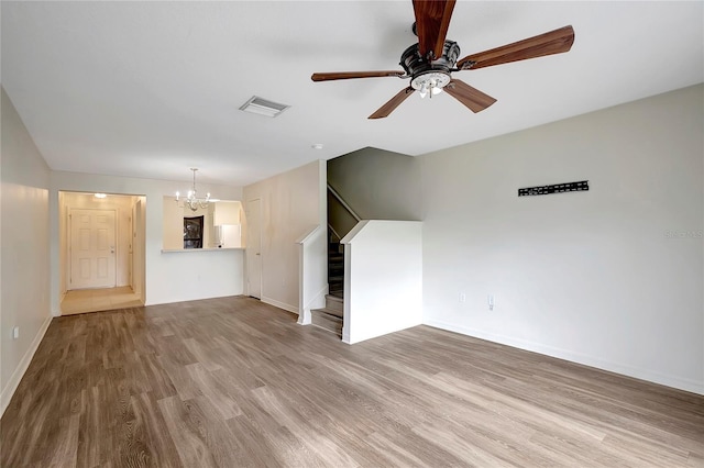 unfurnished living room featuring stairs, a chandelier, wood finished floors, and baseboards
