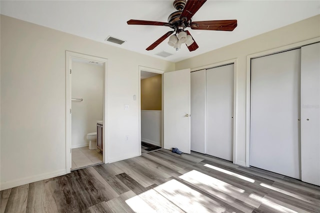 unfurnished bedroom featuring two closets, light wood-style flooring, ensuite bath, and a ceiling fan