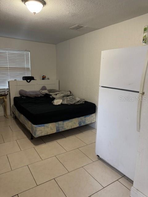 3713 E Clifton St, Tampa, FL 33610 - bedroom with freestanding refrigerator, light tile patterned floors, visible vents, and a textured ceiling