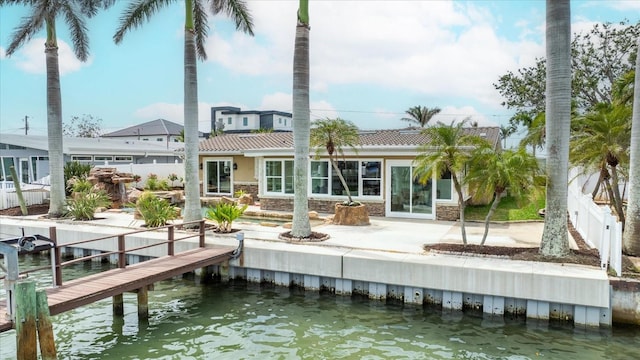 back of property featuring a water view, a patio area, fence, and stone siding