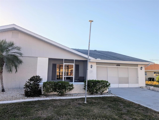 ranch-style house with brick siding, an attached garage, driveway, and a sunroom