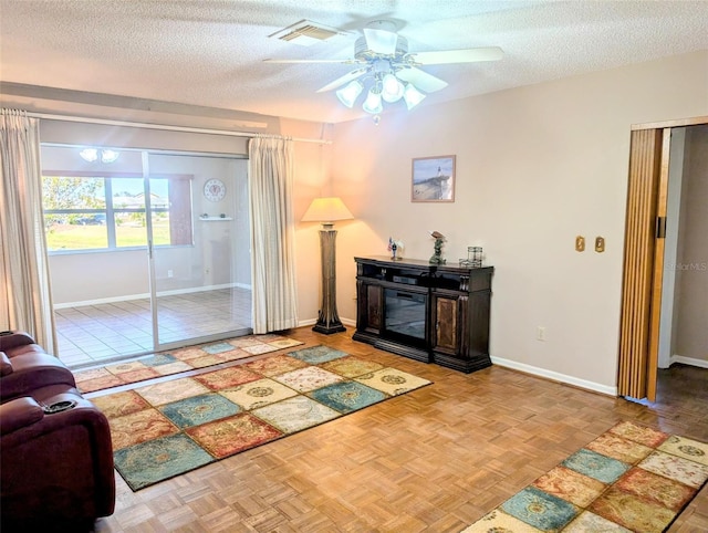 living area featuring a ceiling fan, baseboards, visible vents, and a textured ceiling