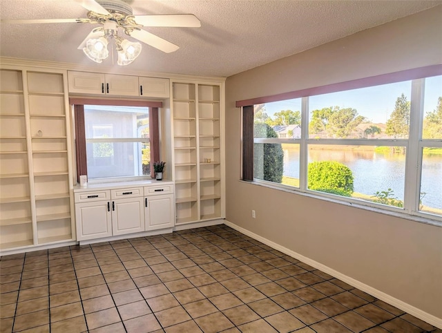unfurnished living room with a textured ceiling, a healthy amount of sunlight, built in shelves, a ceiling fan, and a water view