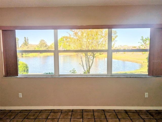 spare room with dark tile patterned flooring, a water view, and baseboards