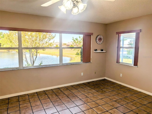 unfurnished room featuring a ceiling fan, a textured ceiling, baseboards, light tile patterned flooring, and a water view
