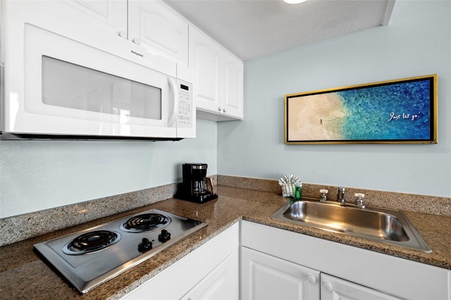 kitchen featuring white microwave, a sink, stainless steel cooktop, white cabinets, and dark countertops